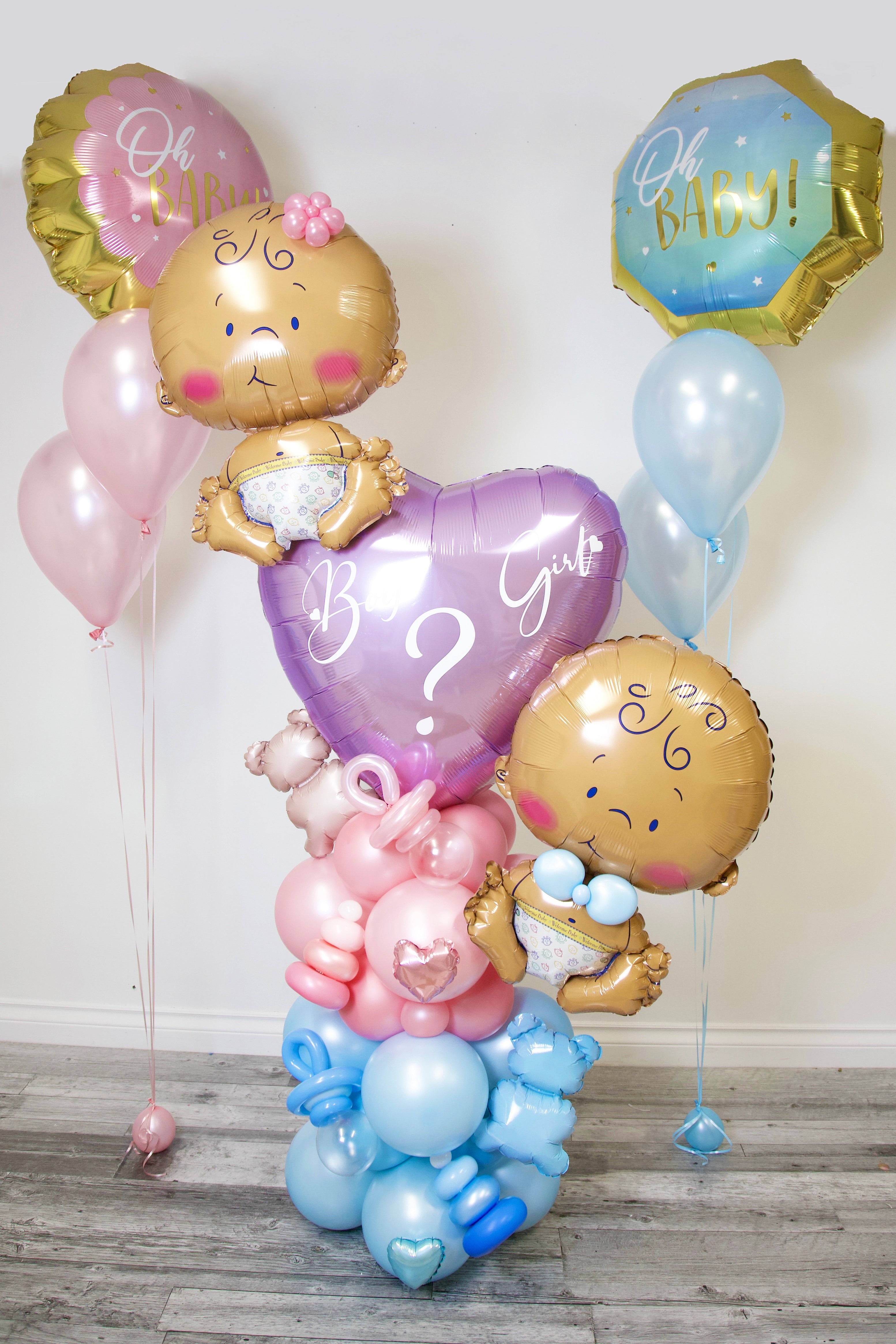 Balloon arrangement with baby-themed balloons and decorations on a wooden floor.
