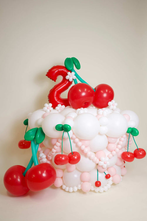 Cherry Birthday Balloon Decor with red cherry balloons, blush and white balloon base, mini flowers, and custom number balloon