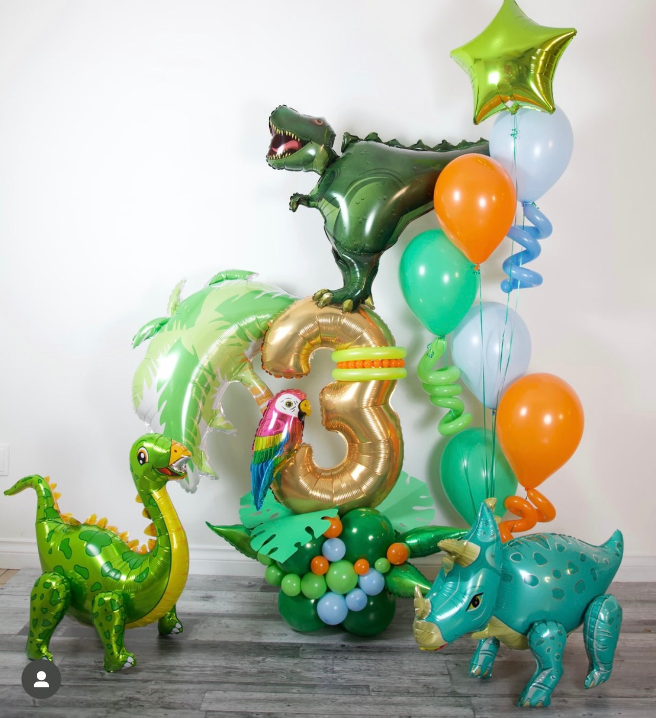Dinosaur-themed balloons with a number 3 and colorful balloons on a wooden floor.