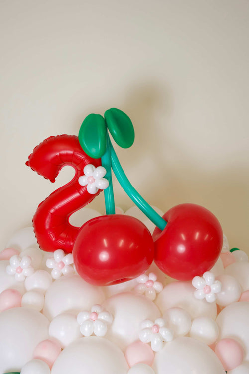Cherry Birthday Balloon Decor with red cherry balloons, blush and white balloon base, mini flowers, and custom number balloon