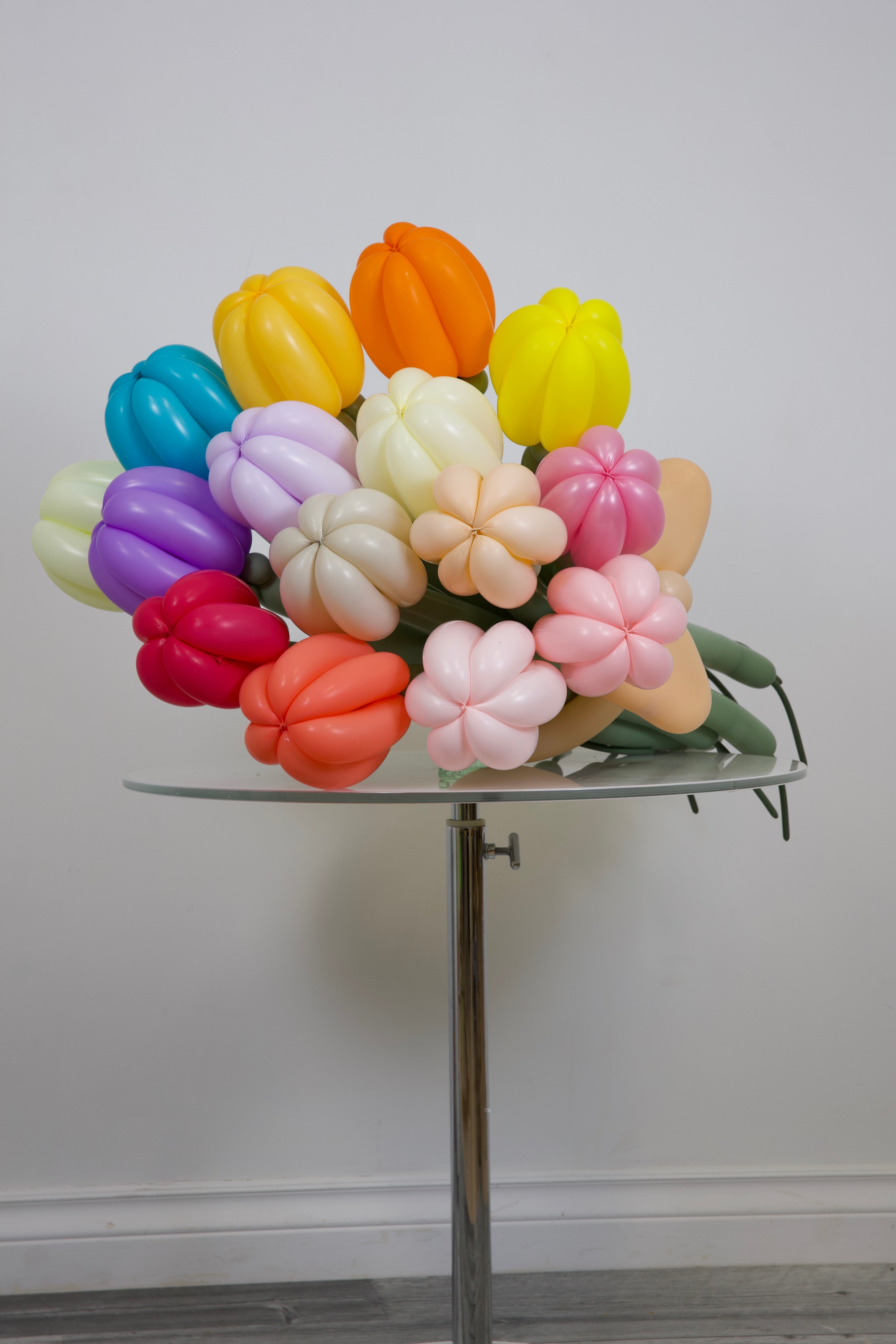 Colorful balloon sculpture resembling a bouquet on a stand against a plain background