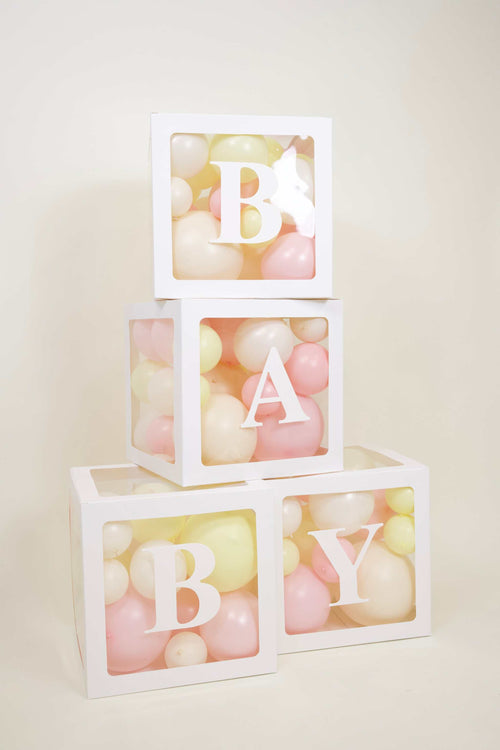 Pastel baby girl balloon boxes with white BABY display, blush balloons, buttercream details, and floral baby shower decor