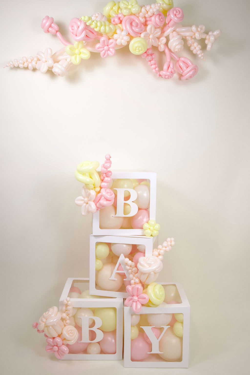 Luxury baby girl balloon box decor with pastel BABY boxes, pink and white balloons, floral accents, and baby shower backdrop styling