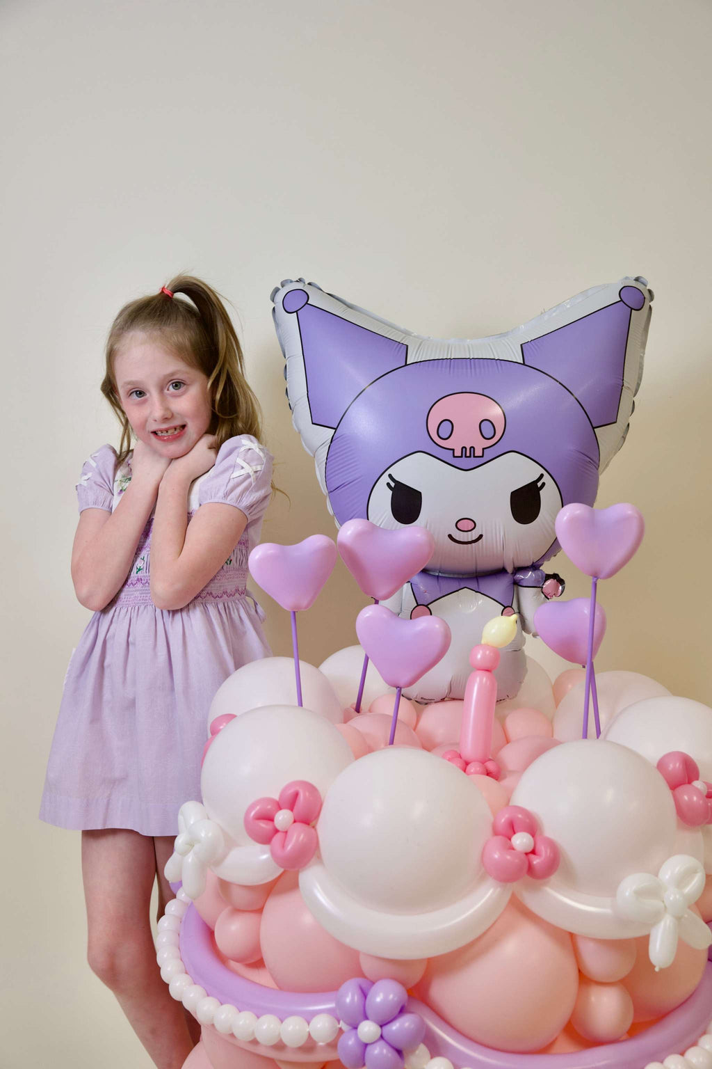 Kuromi-inspired pastel pink balloon cake display with character foil topper and floral accents for birthday centerpiece