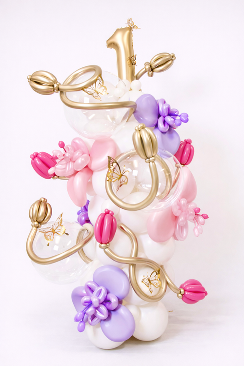 Baby girl birthday balloon decoration with butterfly accents, soft pink balloons, lavender balloons, gold details, and freestanding number display.
