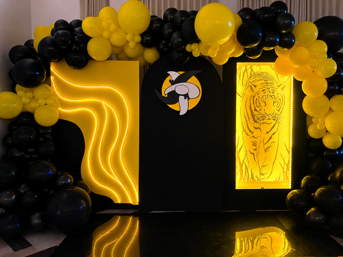 Black and yellow tiger LED backdrop with illuminated wave lights and organic balloon canopy for event installation