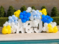 Custom blue, yellow, and white marquee letter balloon installation with greenery accents for outdoor celebrations and events