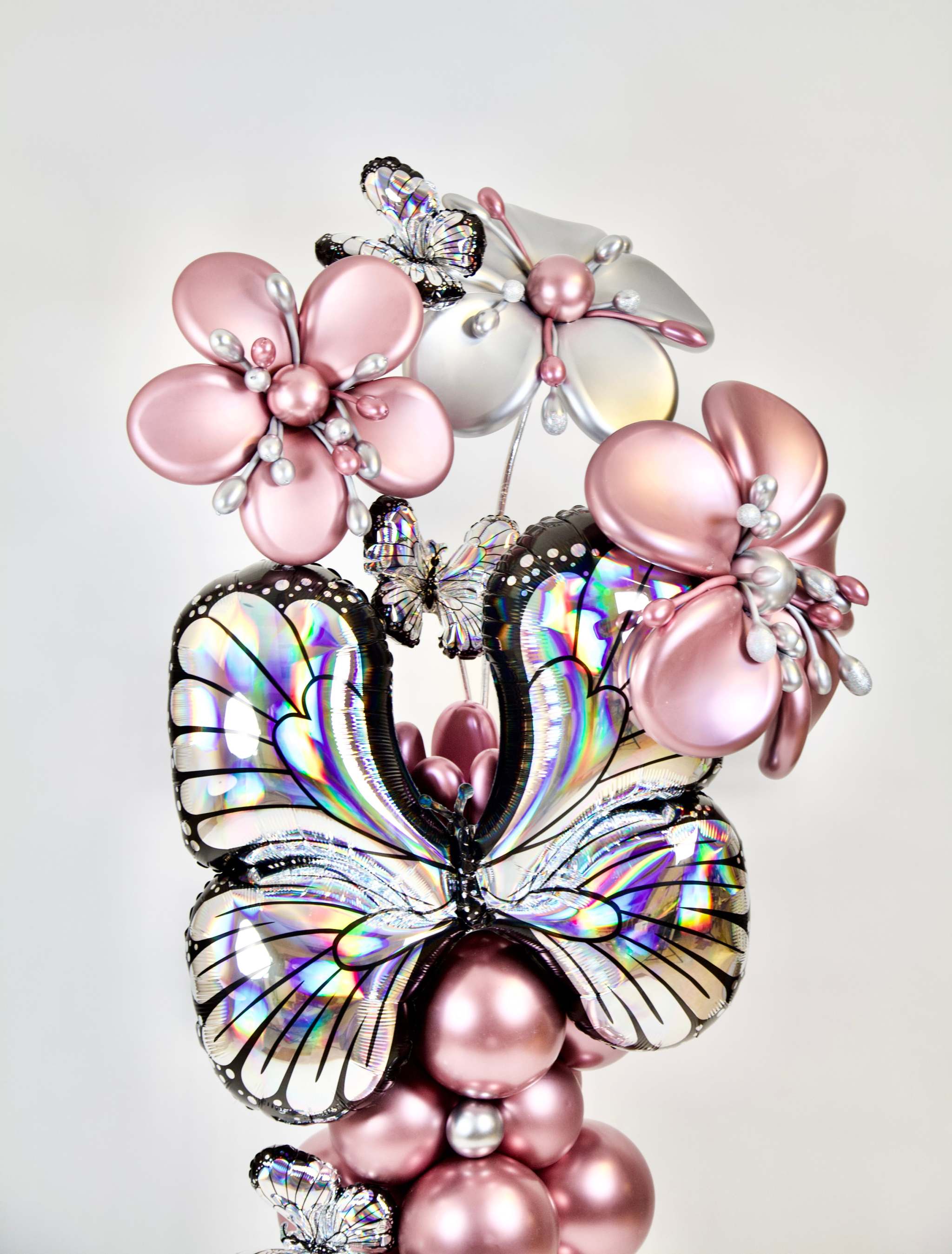 Luxury butterfly balloon decor with metallic rose gold balloon column, silver accents, floral balloon sculptures, and butterfly details