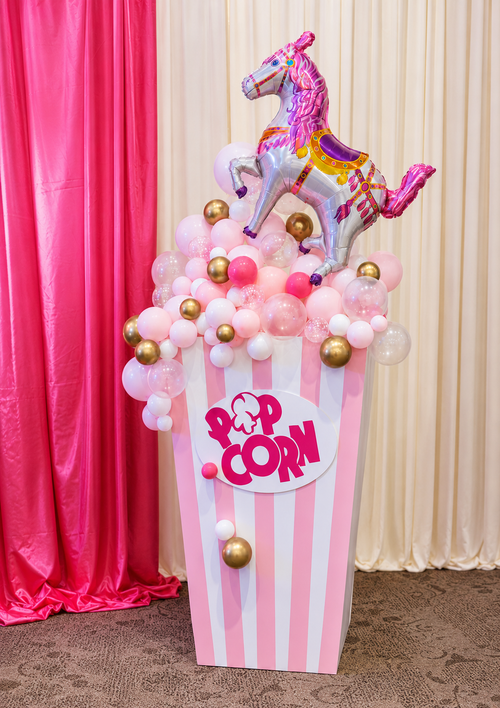 Oversized pink and silver carousel horse balloon with striped popcorn prop and mixed blush pink, white, clear, and gold balloons for children's party display