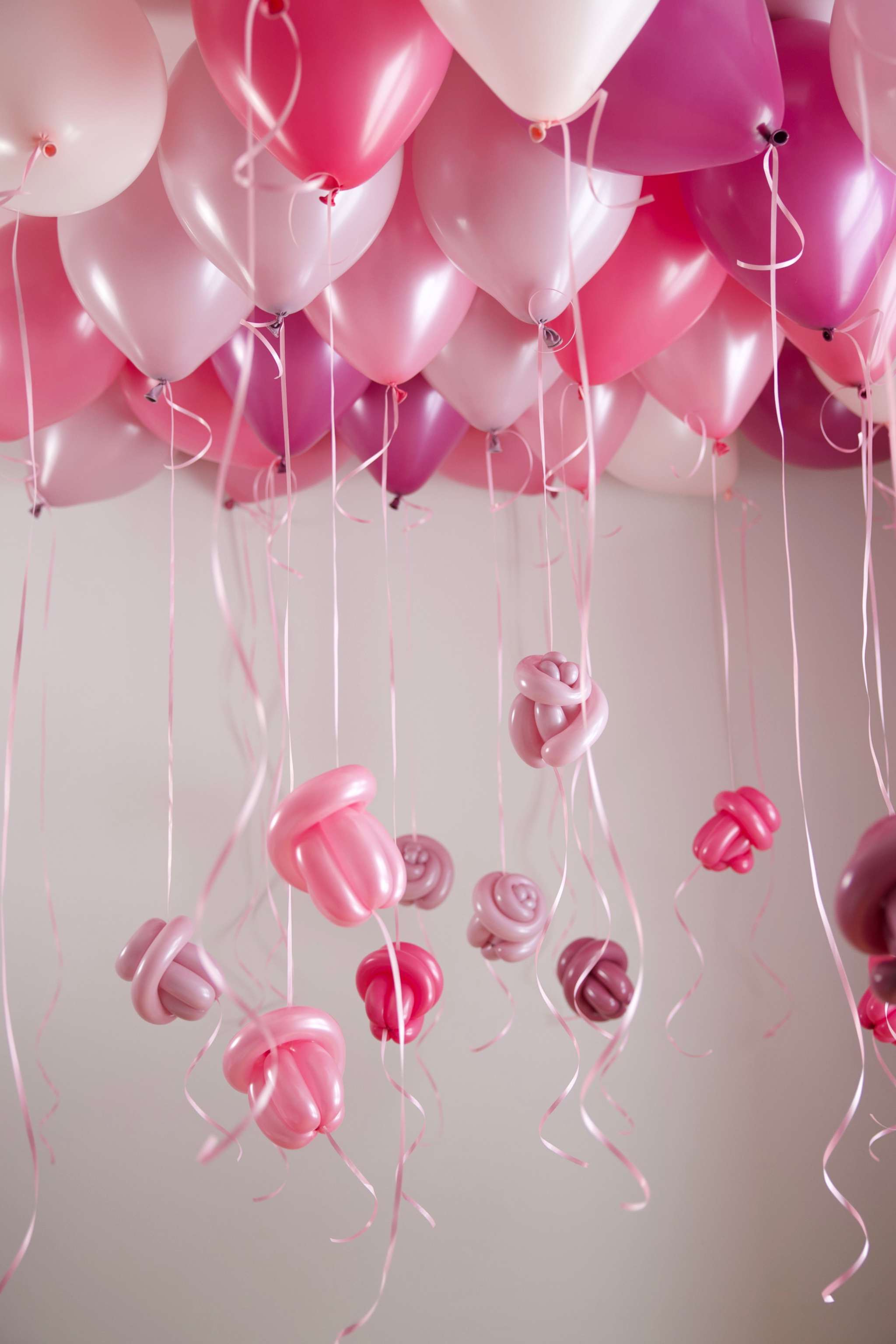 Soft pink and white helium balloons floating from the ceiling with hanging ribbons and balloon flower accents for party decor