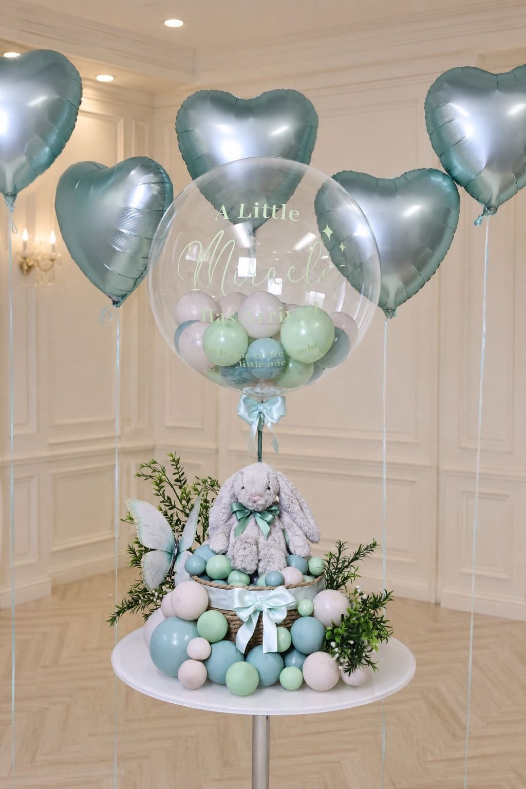 Personalized Little Miracle Bunny Bubble Balloon gift with plush bunny, clear bubble balloon, greenery, and satin bows in a woven basket for newborn celebrations