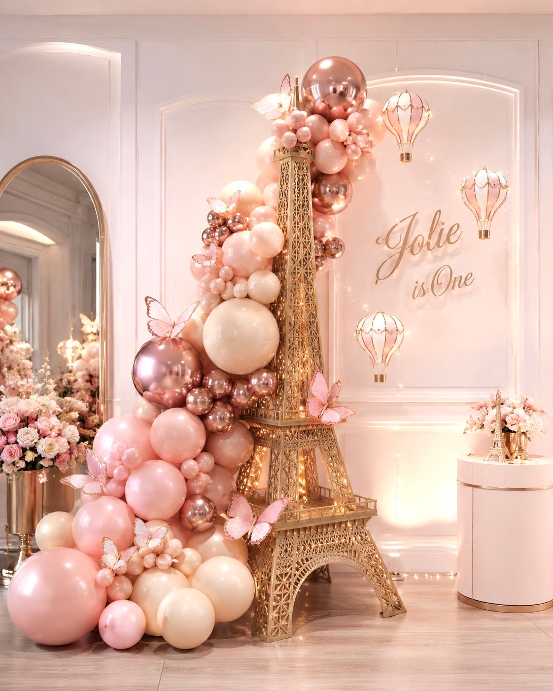 Parisian Butterfly first birthday installation with Eiffel Tower, blush and rose-gold balloons, butterflies, and warm lighting