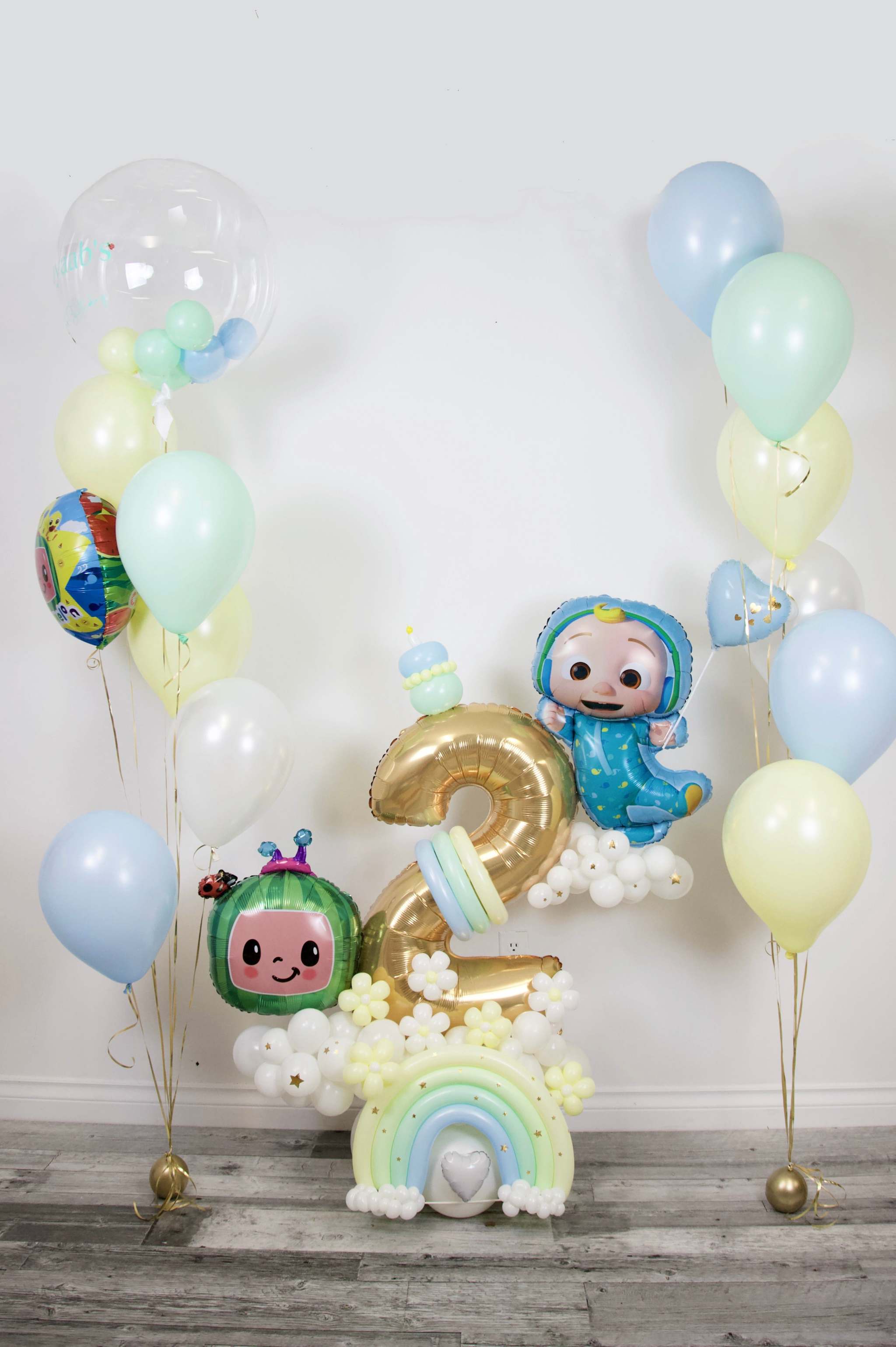 Pastel rainbow birthday balloon display with gold number, cloud base and helium bouquets