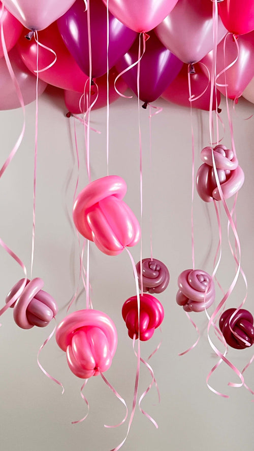 Blush pink ceiling balloon installation with floating rose drops and ribbons for romantic event decor