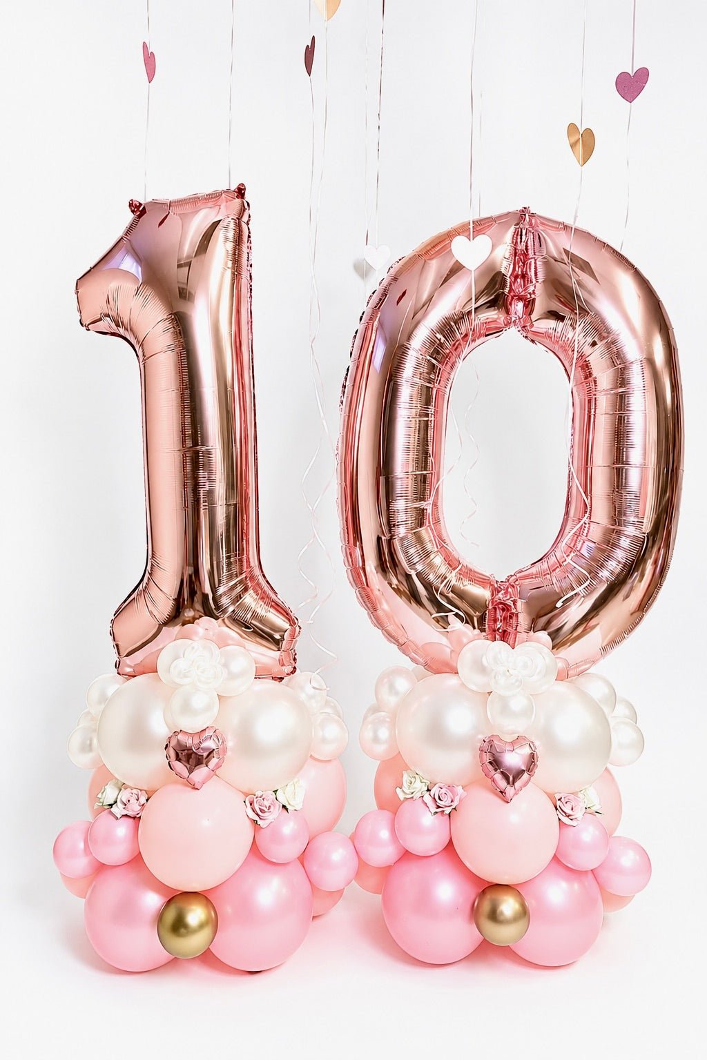 Rose gold number balloon columns with blush balloon bases, custom age digits, mini heart accents and floral details