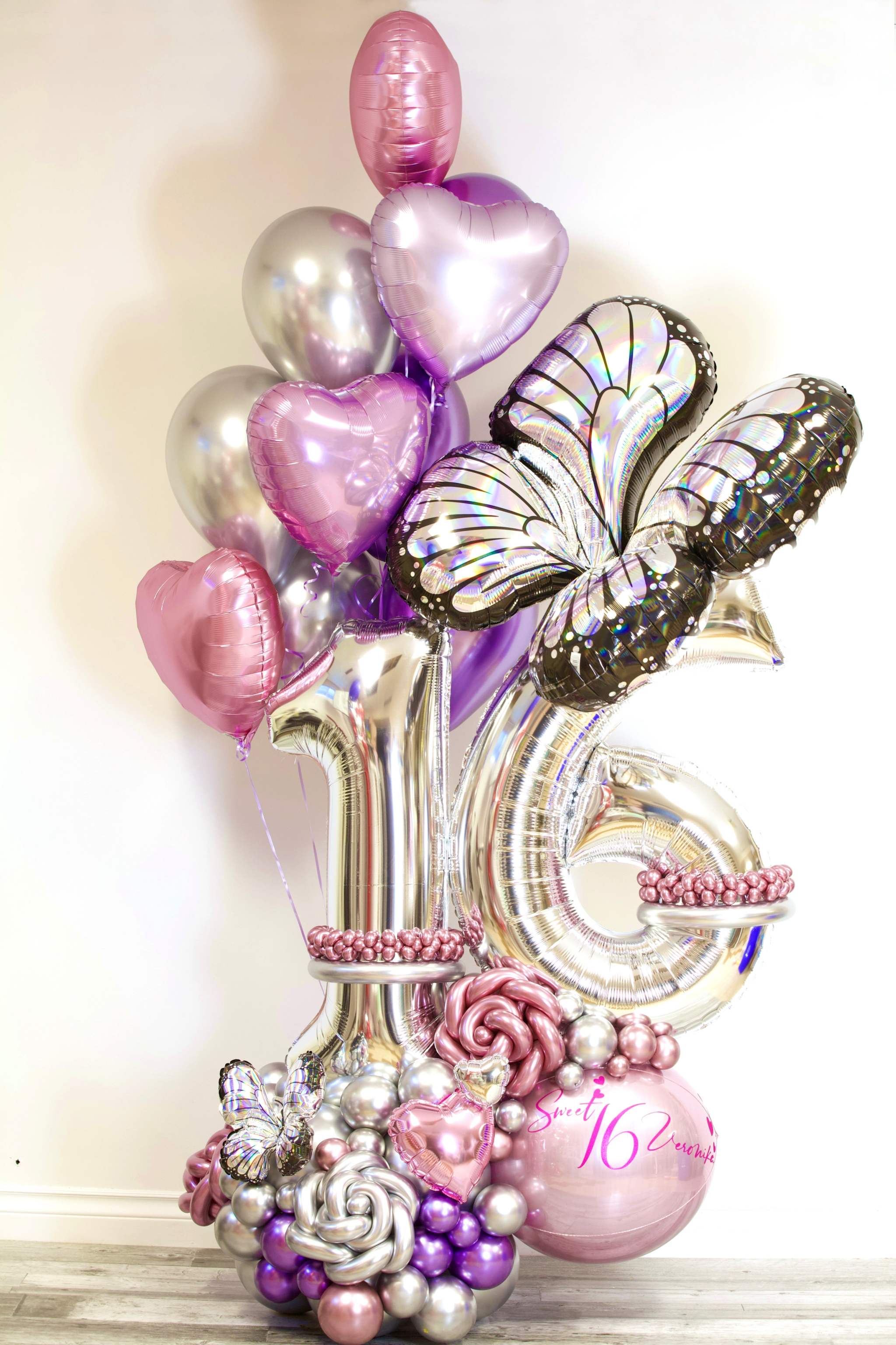 Sweet 16 luxury balloon display with oversized silver age numbers, chrome bouquet, butterfly accents and pearl floral base