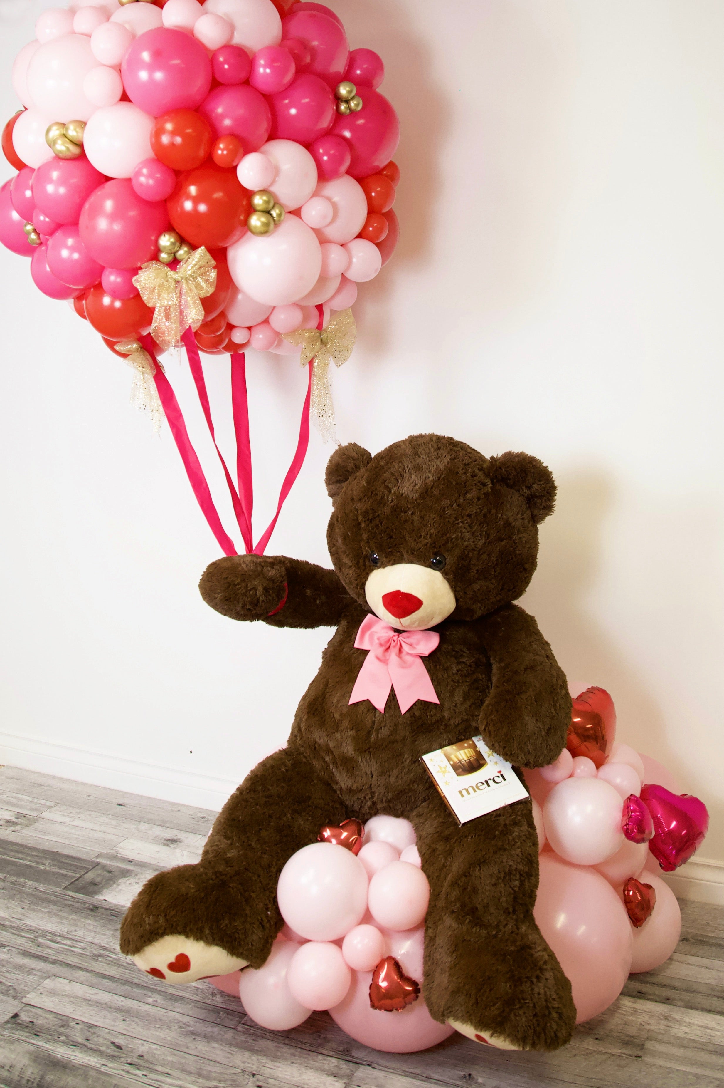 Large teddy bear holding a pink balloon bouquet with romantic balloons and gift arrangement for Valentine’s Day and romantic surprises in Toronto.